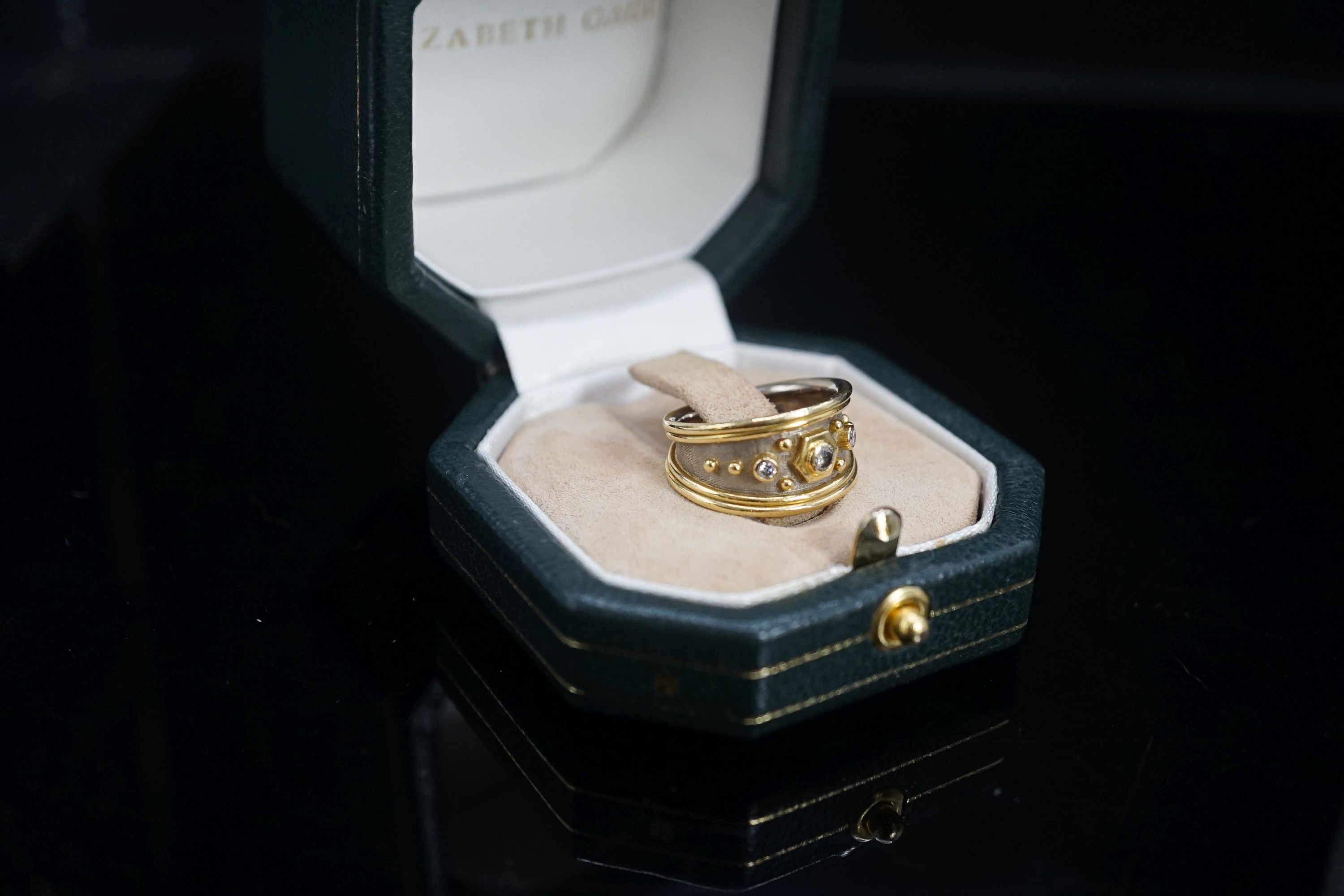 A modern two colour 18ct gold and three stone diamond set dress ring by Elisabeth Gage, size K/L, gross weight 7 grams, with engraved date to shank interior.